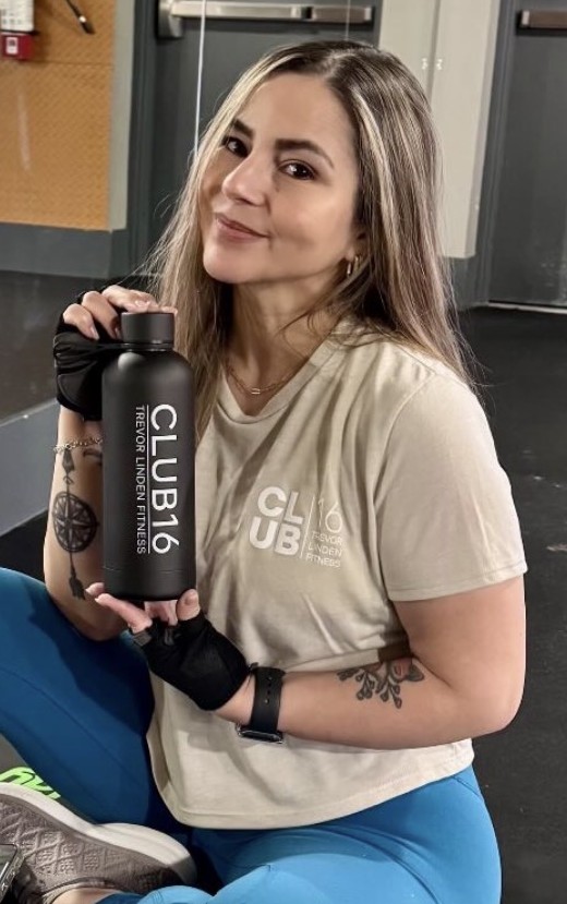 Carla, a Club16 Maple Ridge member of 11 years, sitting on a gym bench holding a Club16 water bottle